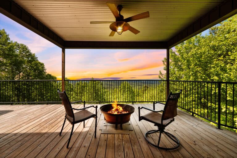 Covered deck with fire pit, ceiling fan, and sunset view over the trees.