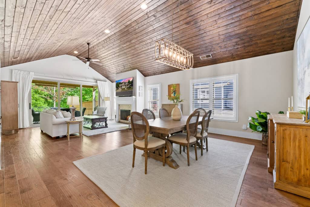 Real estate photograph of an open-concept living and dining area with a wood-paneled ceiling and natural light.