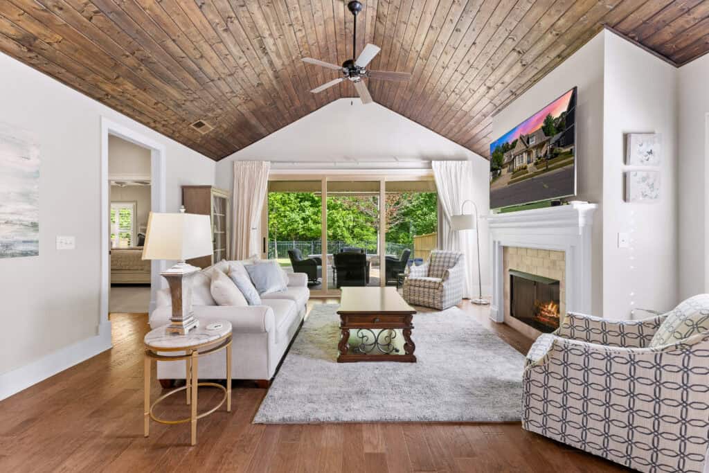 Bright living room with vaulted wood ceiling, fireplace, seating area, and sliding doors to a screened porch.