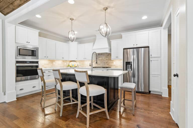 Bright white kitchen with a central island, stainless steel appliances, pendant lights, and bar seating.