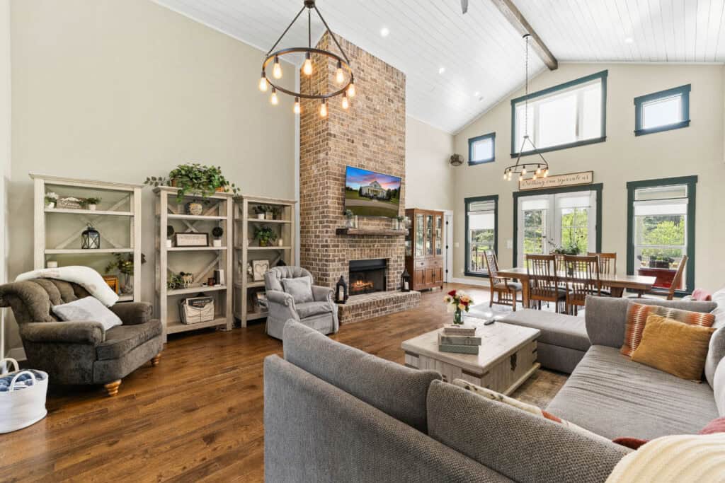 Real estate interior photograph of an open-concept living room with brick fireplace, high ceilings, and dining area