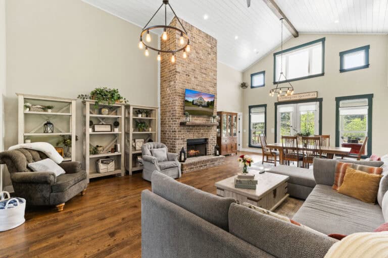 Real estate interior photograph of an open-concept living room with brick fireplace, high ceilings, and dining area