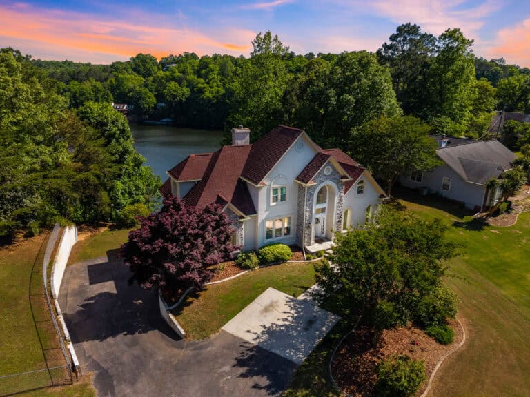Aerial real estate photograph of a large lakeside home surrounded by mature trees and landscaped grounds.