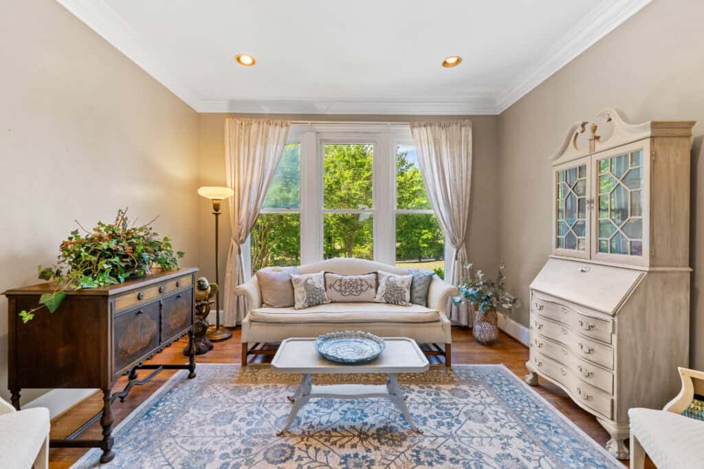 Professionally staged living room photographed for a real estate listing, with a sofa, glass-front cabinet, and large window.