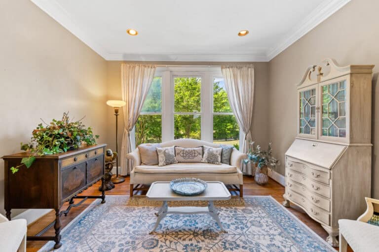 Professionally staged living room photographed for a real estate listing, with a sofa, glass-front cabinet, and large window.