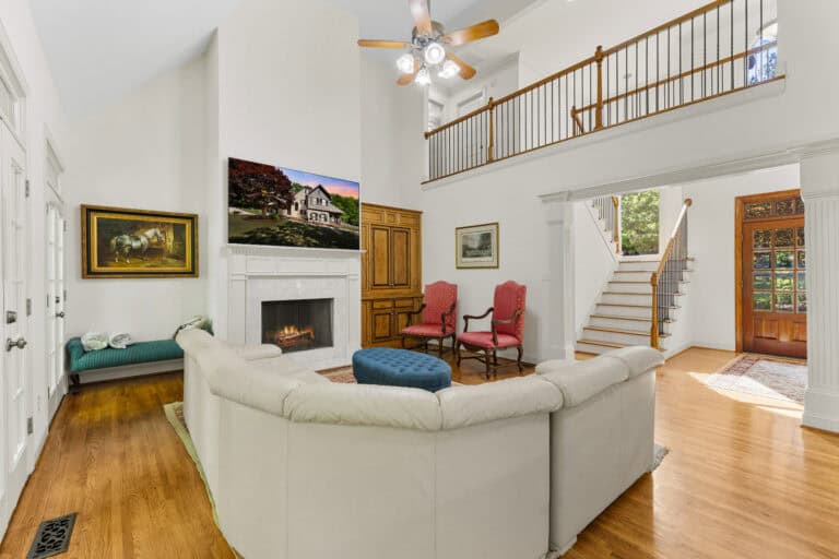 Bright open-concept living room and foyer with fireplace, staircase, balcony, and hardwood floors.