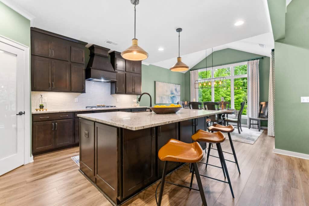Professional real estate photograph of a modern kitchen with dark cabinetry, island seating, and large windows.