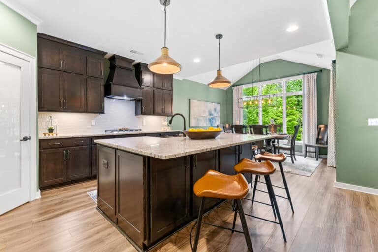 Professional real estate photograph of a modern kitchen with dark cabinetry, island seating, and large windows.