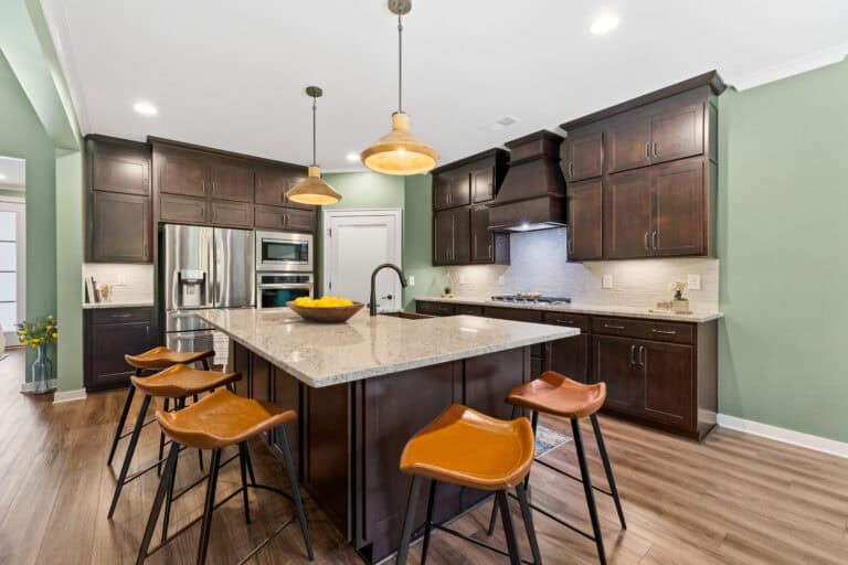 Professional real estate photograph showcasing a modern kitchen with dark wood cabinetry, island, pendant lighting, and seati