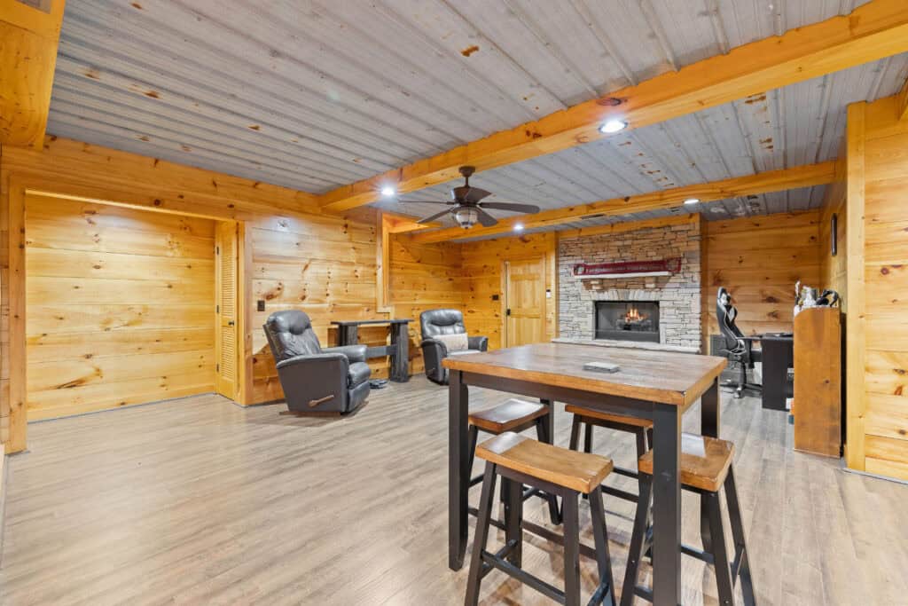 Real estate interior photograph of a wood-paneled living area with fireplace, seating, and bar-height dining table.