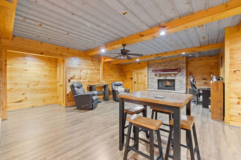 Real estate interior photograph of a wood-paneled living area with fireplace, seating, and bar-height dining table.