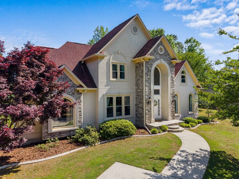 Professional exterior real estate photograph of a large stone-and-stucco home with landscaped grounds.
